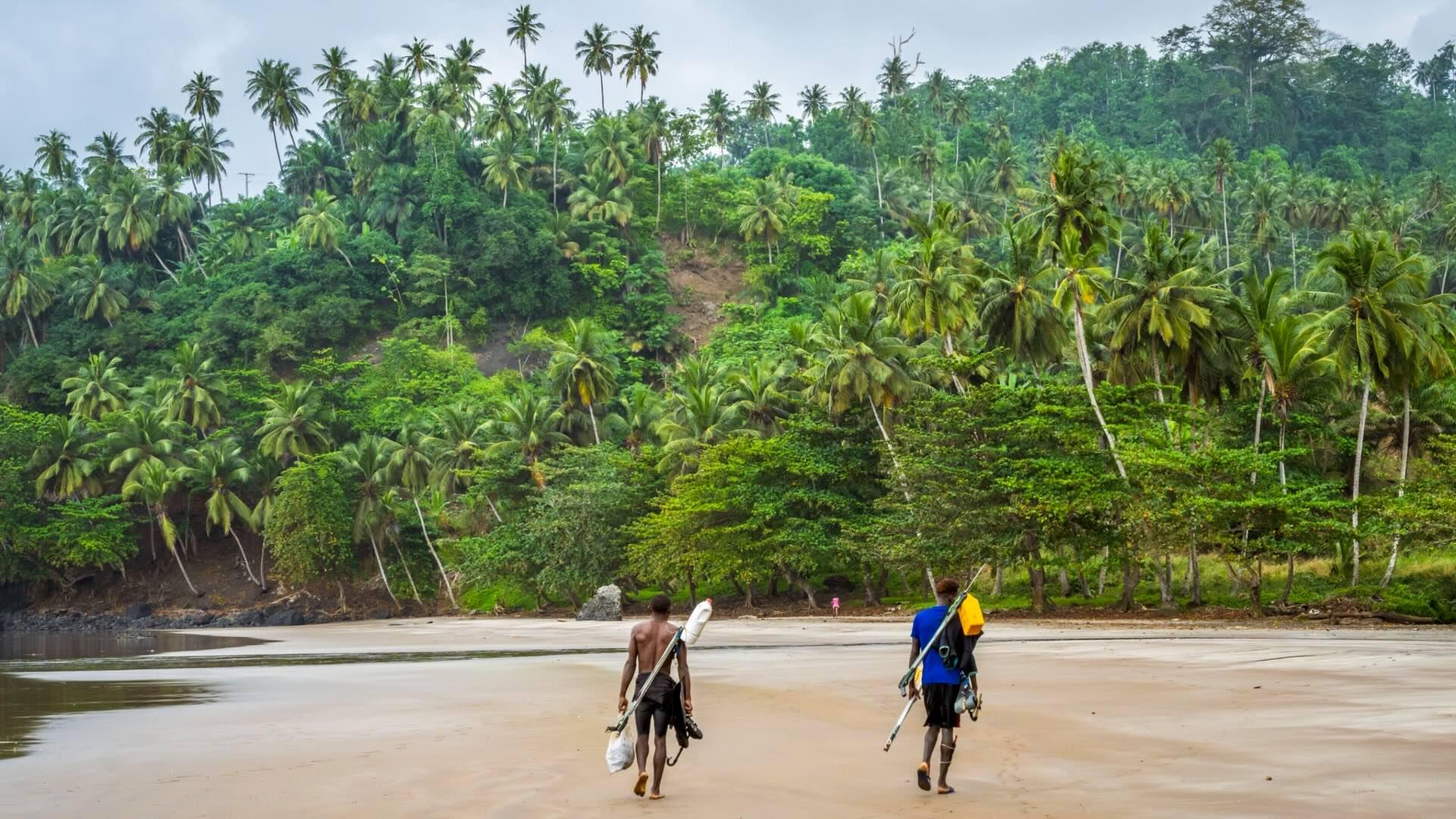 Two local man walking along a beach in Sao Tome with forest in the background. 